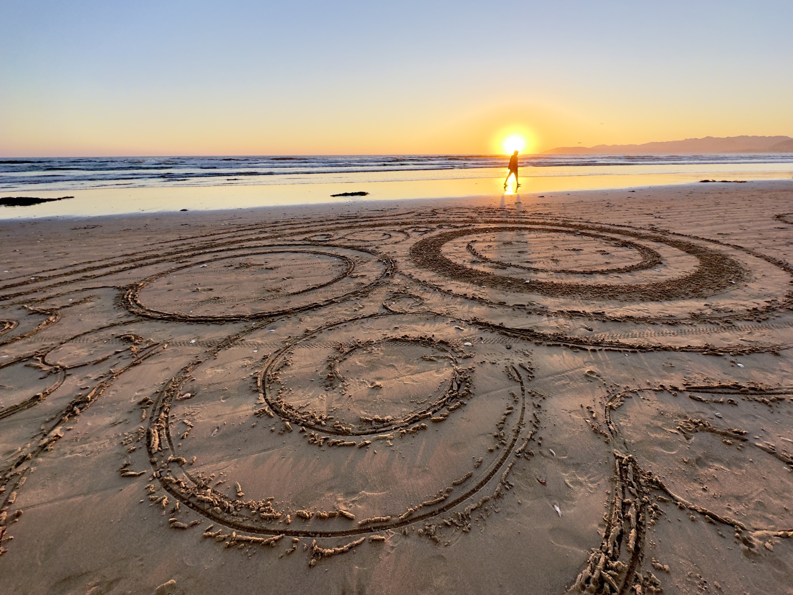 Sand swirls and beach walker at sunset.