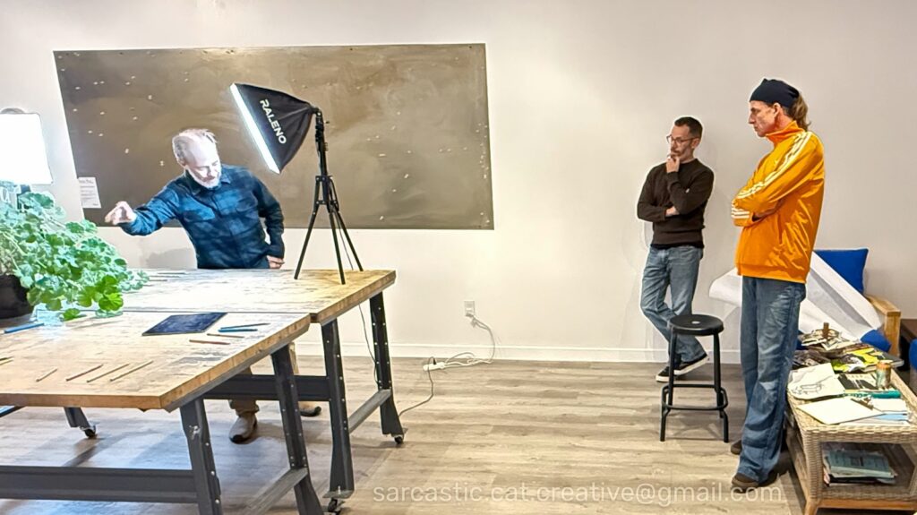 Joe gestures at a subject under bright light while other people look on.