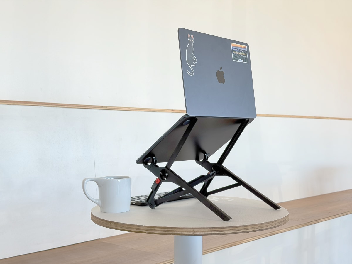 Laptop against a white wall, propped up on a round table with a narrow stand
